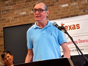 man in blue shirt and glasses speaking at a podium